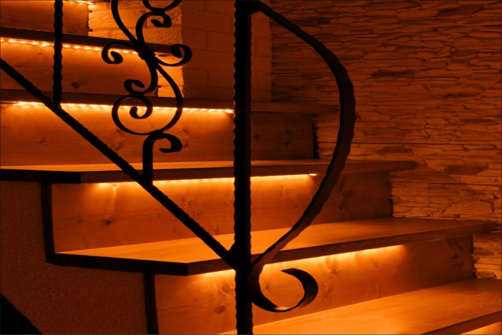 Orange LED lighting wooden stairs illuminated with LED strips. Effective LED lighting of smart stairs.